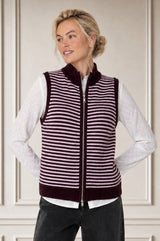 Model wearing the Aspiga Merino Wool Stripe Zip Through Gilet in Burgundy/Pink over a white blouse with black trousers, front view