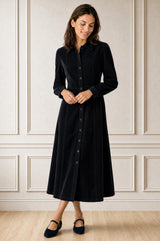 Model wearing the Aspiga A-Line Cord Dress in Navy, a corduroy button-front shirt dress with a collar, long sleeves and a tie waist, front view