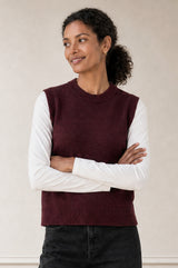 Model wearing the Aspiga Merino Wool Knitted Short Tank in Burgundy layered over a white long-sleeve top, arms crossed