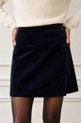 Model wearing the Aspiga Corduroy Wrap Mini Skirt in Dark Navy, a wrap-style corduroy mini skirt with a button fastening, front view