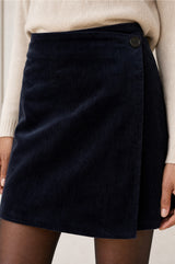 Model wearing the Aspiga Corduroy Wrap Mini Skirt in Dark Navy, a wrap-style corduroy mini skirt with a button fastening, alternate view