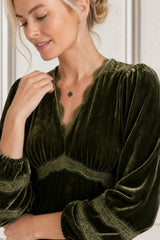 Close-up of a model wearing the Aspiga Lorna Lace Velvet Dress in Dark Olive, showing the lace-trimmed V-neck and gold necklace