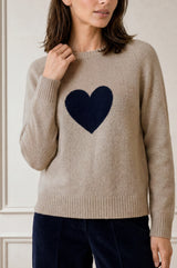 Model wearing the Aspiga Cashmere Crew Neck Heart Jumper in Oat/Navy, close-up with hand at collar