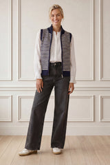 Model wearing the Aspiga Merino Wool Stripe Zip Through Gilet in Navy/Off White over a white blouse with black trousers, full-length front view, smiling