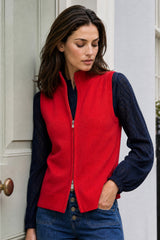 Model wearing the Aspiga Merino Wool Zip Through Gilet in Red over a navy lace top with jeans, leaning against a door
