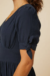 Close-up of a navy dress showing the short sleeve with a delicate tie detail and gathered fabric at the shoulder.