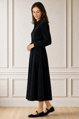 Model wearing the Aspiga A-Line Cord Dress in Navy, a corduroy button-front shirt dress with a collar, long sleeves and a tie waist, alternate view