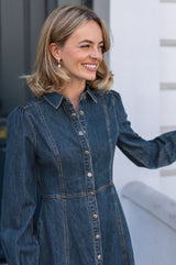 Close-up of a model wearing the Aspiga A-Line Denim Midi Dress in Indigo, smiling and reaching for her hair