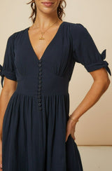 Close-up of a navy midi dress with a deep V-neckline, button-down front, fitted waist, and short sleeves with tie details.