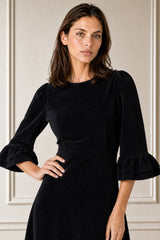 Close-up of a smiling model wearing the Aspiga Elizabeth Stretch Corduroy Midi Dress in Black, hand on hip