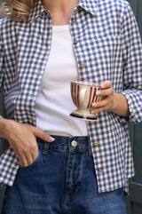 Close-up of a model wearing the Aspiga Classic Gingham Shirt in Blue/White, holding a striped teacup