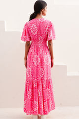 Woman wearing a pink floral dress with short floaty sleeves and ruched waistband back