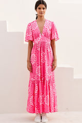 Woman wearing a pink floral dress with short floaty sleeves and v neckline on a white background