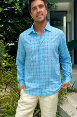 A man wearing a hyacinth blue to turquoise colored geometric patterned organic cotton shirt with a collar.