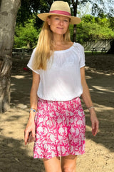 Woman outdoors wearing a pink and white floral smocked mini skirt with ruffle hem, paired with a white short-sleeve blouse and a straw hat with a pink band.