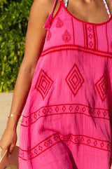 Zoom in of a woman wearing a pink and red embroidered cotton dress with a scoop neckline and spaghetti tie straps, standing on a beach