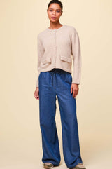 Wide-leg denim trousers with drawstring waist and relaxed fit, styled with a beige cardigan and trainers.