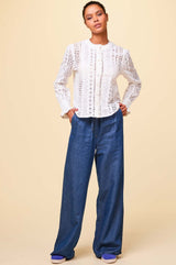 Wide-leg denim trousers with relaxed fit, drawstring waist and side pockets, styled with a white broderie anglaise blouse and trainers.