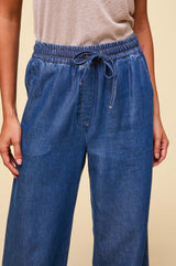 Close-up of woman wearing wide-leg denim trousers with elasticated drawstring waist and side pockets, paired with a beige top.