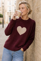 Model wearing the Aspiga Cashmere Crew Neck Heart Jumper in Burgundy/Oat, drinking a takeaway coffee outdoors