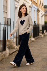 Model wearing the Aspiga Cashmere Crew Neck Heart Jumper in Oat/Navy with navy corduroy trousers, walking outdoors on a street