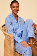 Woman wearing a light blue button-up pyjama set with a small navy floral print and contrast piping, paired with tan shearling slippers.
