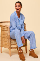 Woman wearing a light blue button-up pyjama set with a small navy floral print and contrast piping, paired with tan shearling slippers.