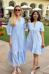 Two woman pictured wearing a light blue and white striped midi dress with delicate embroidery and a tiered hem. One of the dresses is a shorter length version, with shorter sleeves.