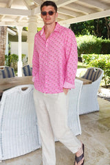 A man wearing sunglasses and a periwinkle pink/rust colored long-sleeved cotton shirt with a classic collar paired with neutral linen trousers