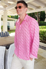 A zoom in of a man wearing sunglasses and a periwinkle pink/rust colored long-sleeved cotton shirt with a classic collar paired with neutral linen trousers
