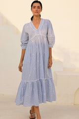 Woman wearing a light blue and white striped midi dress with delicate embroidery, puffed sleeves, and a tiered hem.