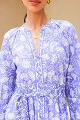 A model wearing a long sleeve, midi length blue and white floral print dress with a deep V-neck and blouson sleeves with a tie belt around the waist
