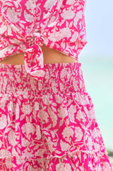 Close-up of a bright pink and white floral smocked mini skirt with ruffle detail, paired with a matching tied shirt.