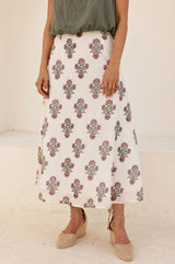 Woman wearing a white midi skirt with a pink and green floral block print pattern, paired with a green top and beige espadrille wedges.