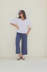 A person standing wearing navy wide leg linen cropped trousers with a white top, paired with beaded sandals.