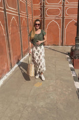 Video of Lucy wearing wearing a white maxi skirt with pink and green floral block print, styled with a olive green top, white trainers and a beach bag.