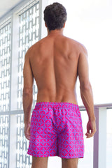 Man seen from behind wearing bright pink and blue patterned swim shorts.