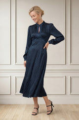 Model wearing the Aspiga Satin Jacquard Spot Dress in Navy with black heels, full-length front view, smiling