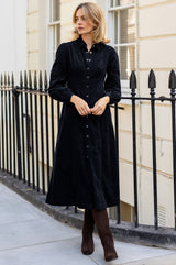 Model wearing the Aspiga A-Line Baby Cord Dress in Navy, a corduroy button-front shirt dress with a collar and puff-shoulder long sleeves, full-length front view