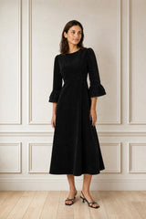 Model wearing the Aspiga Elizabeth Stretch Corduroy Midi Dress in Black with strappy heels, full-length front view, looking to the side