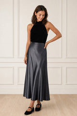 Model wearing the Aspiga Satin Slip Skirt in Slate with a black halter top and black flats, full-length front view, smiling