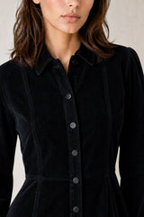 Model wearing the Aspiga A-Line Cord Dress in Navy, a corduroy button-front shirt dress with a collar, long sleeves and a tie waist, alternate view