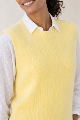 Model wearing the Aspiga Alpaca Blend Knitted Short Tank in Pale Yellow, a ribbed knit sweater vest layered over a white blouse, alternate view
