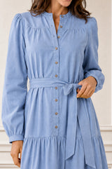 Model wearing the Aspiga Baby Cord Midi Dress in Ice Blue, a light blue corduroy belted shirt dress with long sleeves and a collar, alternate view