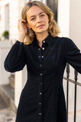Close-up of a model wearing the Aspiga A-Line Baby Cord Dress in Navy, a corduroy button-front shirt dress with a collar and puff-shoulder long sleeves