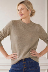 Model wearing the Aspiga Merino Wool Crew Neck Jumper in Oatmeal with dark denim jeans, hands on hips, smiling