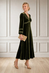 Model wearing the Aspiga Lorna Lace Velvet Dress in Dark Olive with a gold clutch, full-length side view, smiling