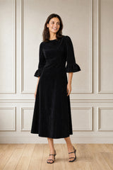 Model wearing the Aspiga Elizabeth Stretch Corduroy Midi Dress in Black with strappy heels, full-length side view