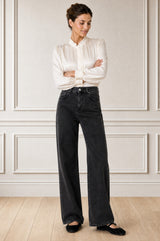 Model wearing the Aspiga Relaxed Straight Denim Jean in Black with a cream blouse, full-length front view, arms crossed