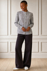 Model wearing the Aspiga Cosima Embroidered Blouse in Chocolate/White tucked into dark trousers, full-length front view against a paneled wall